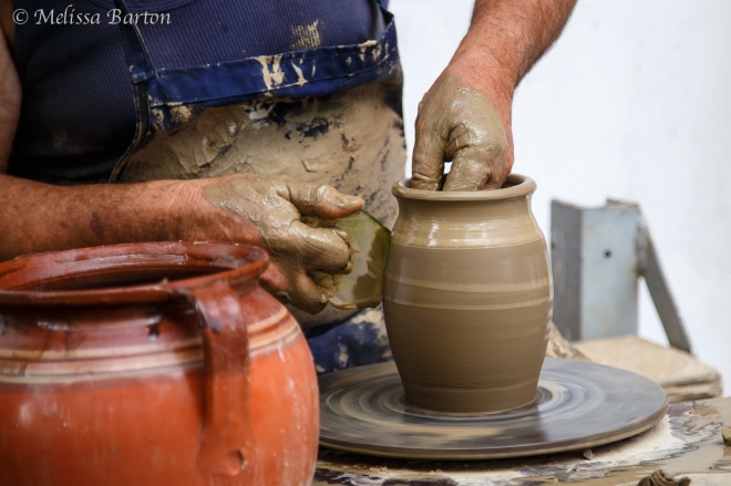 Closeup of a potter's hands shaping a wet clay vase.